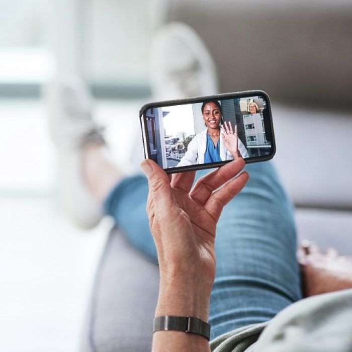 Frau sitzt mit Smartphone zu Hause und spricht per Videotelefonie mit einer Ärztin