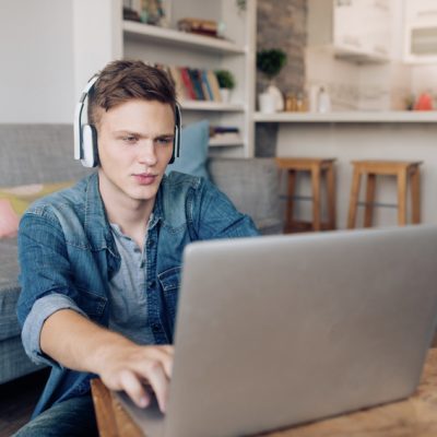 Ein junger Mann mit Kopfhörern schaut auf einen Laptop
