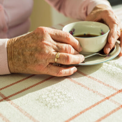 ältere Dame sitzt mit Teetasse alleine am Tisch